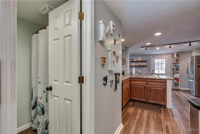 kitchen featuring brown cabinetry, wood finished floors, freestanding refrigerator, a peninsula, and light countertops