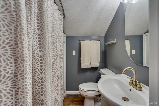 full bath featuring visible vents, vaulted ceiling, a sink, a textured ceiling, and wood finished floors