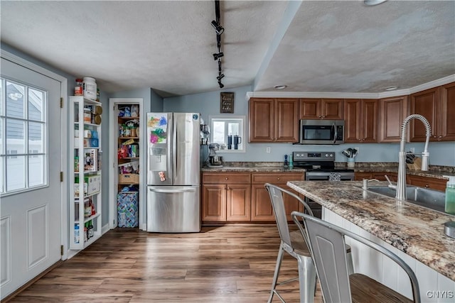 kitchen featuring stainless steel appliances, light stone countertops, a sink, a textured ceiling, and wood finished floors