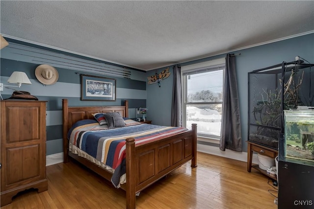 bedroom featuring light wood-type flooring, crown molding, a textured ceiling, and baseboards