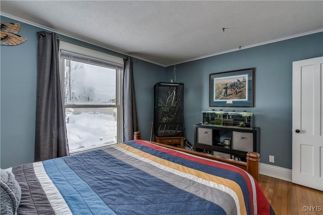 bedroom with a textured ceiling, wood finished floors, baseboards, and ornamental molding
