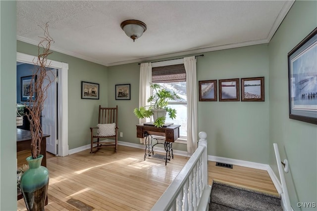 interior space featuring visible vents, baseboards, ornamental molding, a textured ceiling, and light wood-style flooring