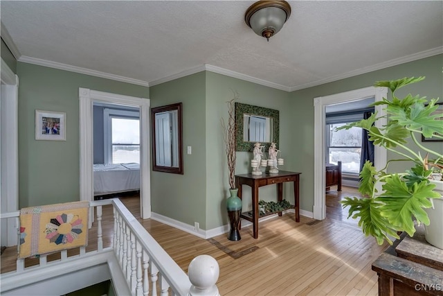corridor with light wood-style flooring, a textured ceiling, baseboards, and ornamental molding