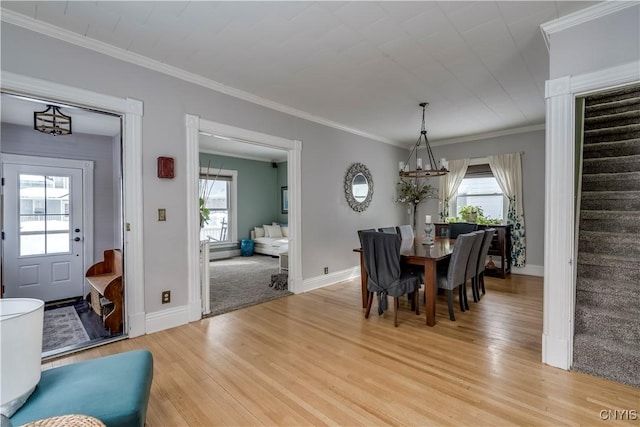 dining room featuring light wood-type flooring, a healthy amount of sunlight, crown molding, and stairs