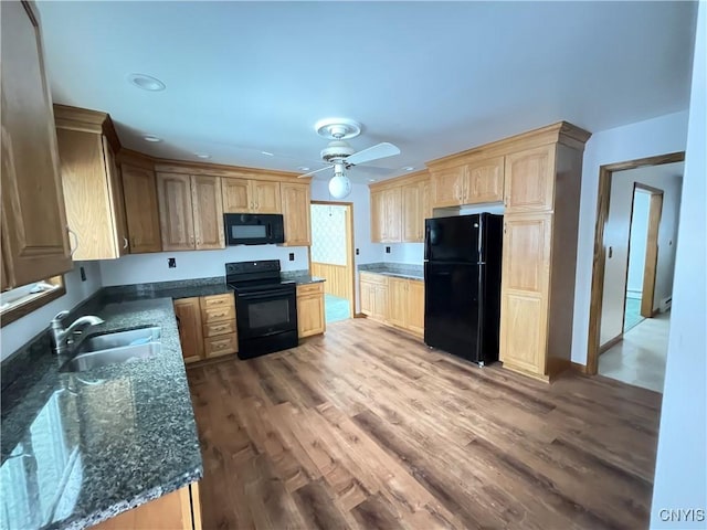 kitchen with black appliances, wood finished floors, dark stone countertops, and a sink