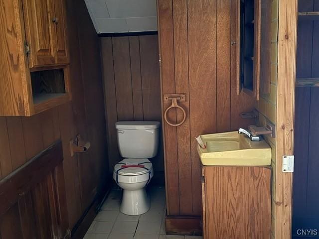 half bath featuring toilet, tile patterned floors, wooden walls, and vanity