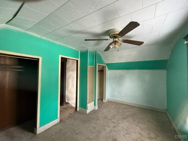 unfurnished bedroom featuring carpet, vaulted ceiling, baseboards, and ceiling fan