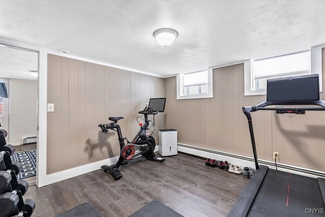 workout room featuring baseboards, baseboard heating, and wood finished floors