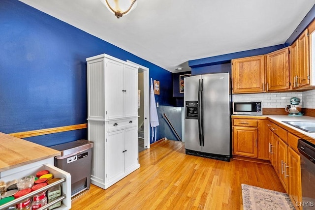 kitchen featuring stainless steel appliances, brown cabinetry, backsplash, and light wood-style floors