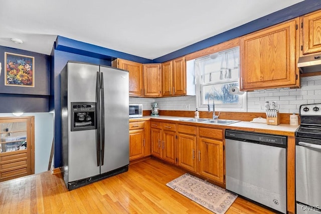 kitchen with light wood finished floors, appliances with stainless steel finishes, light countertops, under cabinet range hood, and a sink