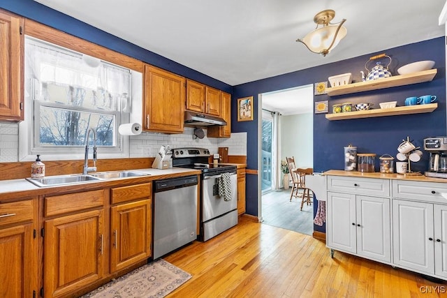 kitchen with under cabinet range hood, stainless steel appliances, a sink, light wood-style floors, and tasteful backsplash