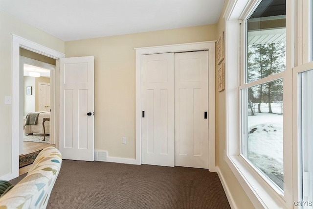 bedroom with a closet, dark carpet, visible vents, and baseboards