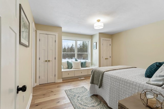 bedroom featuring baseboards, visible vents, light wood finished floors, and two closets