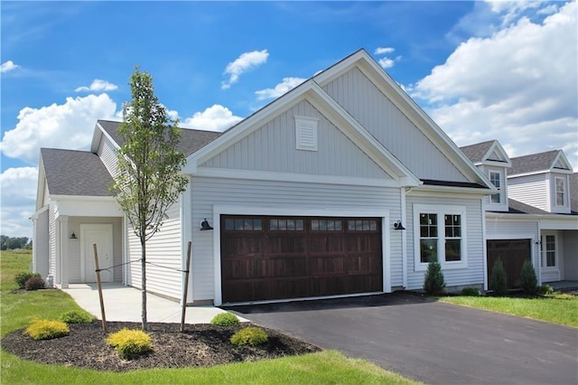 view of front facade with board and batten siding, driveway, a shingled roof, and an attached garage