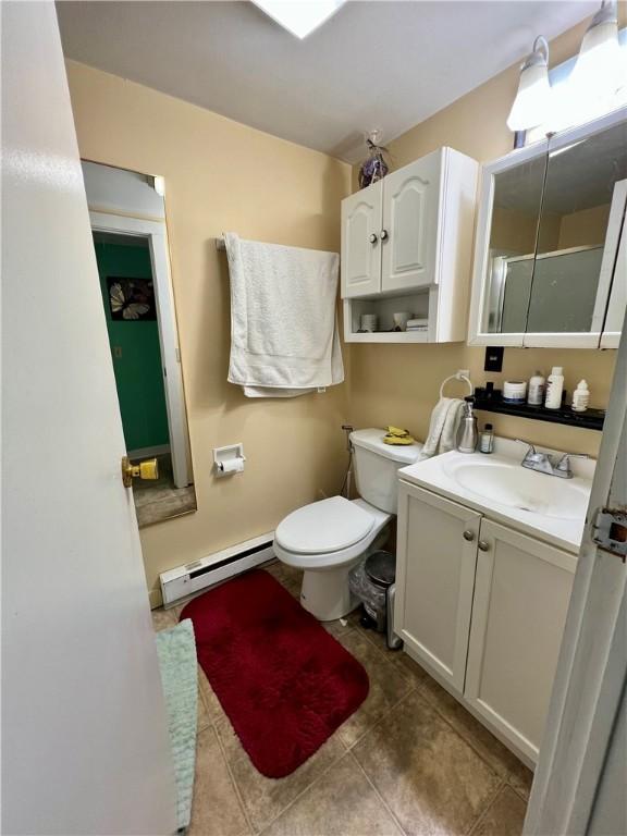 full bath with toilet, a shower with door, a baseboard radiator, tile patterned floors, and vanity