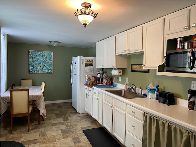 kitchen featuring a sink, baseboards, white cabinets, light countertops, and stainless steel microwave