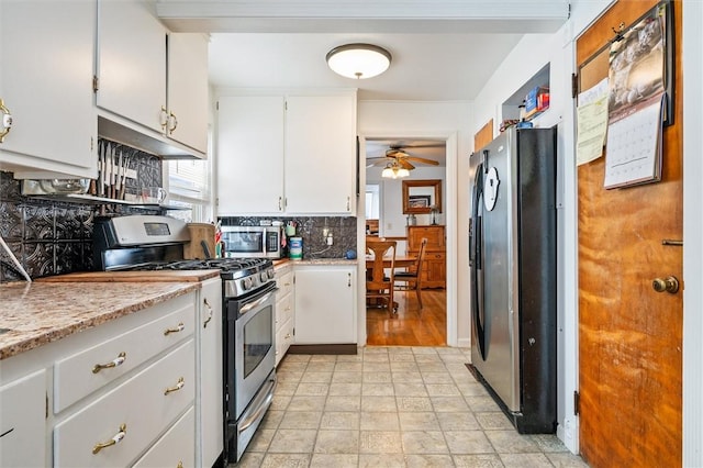 kitchen with decorative backsplash, a ceiling fan, light stone countertops, stainless steel appliances, and white cabinetry