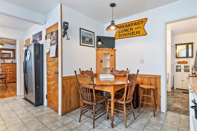 dining area with ceiling fan, stone finish floor, wainscoting, and wooden walls