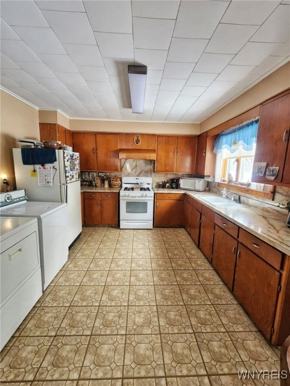 kitchen with white appliances, brown cabinets, washing machine and clothes dryer, light countertops, and a sink