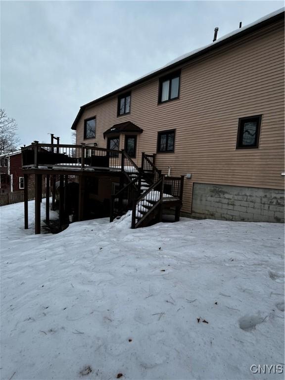 snow covered rear of property featuring stairway and a wooden deck