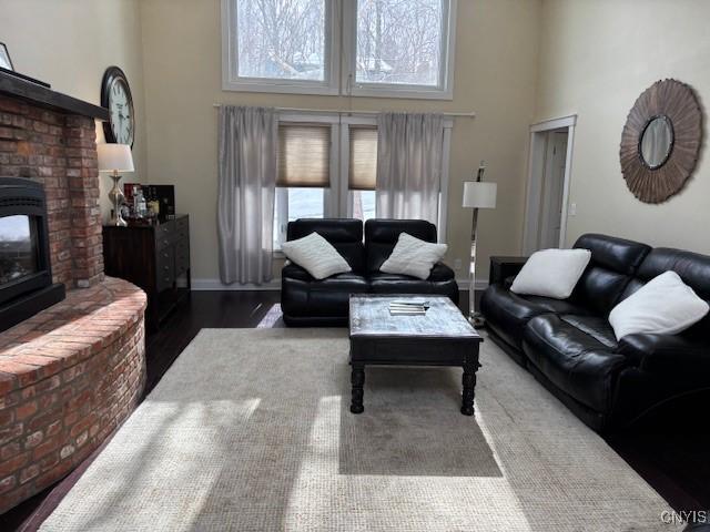 living area featuring a high ceiling, a fireplace, wood finished floors, and baseboards