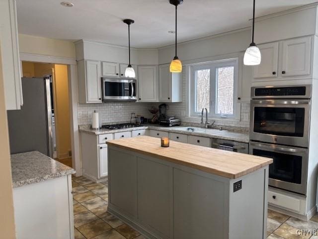 kitchen featuring stainless steel appliances, butcher block countertops, a kitchen island, a sink, and decorative backsplash