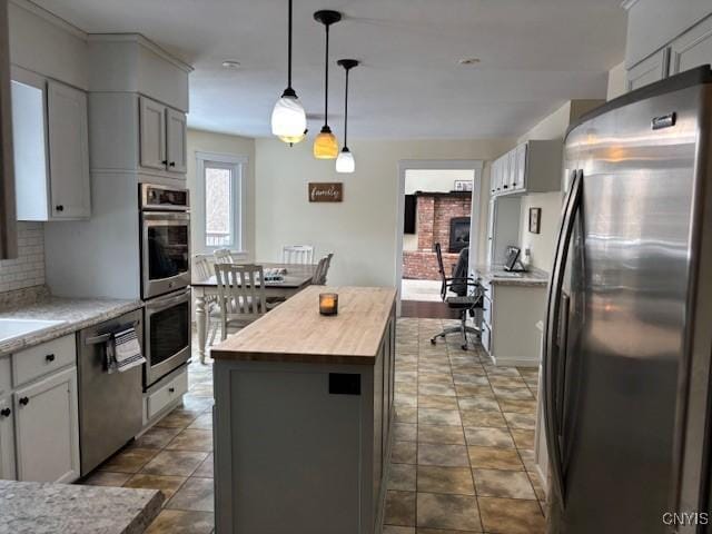 kitchen with pendant lighting, stainless steel appliances, wooden counters, backsplash, and a kitchen island