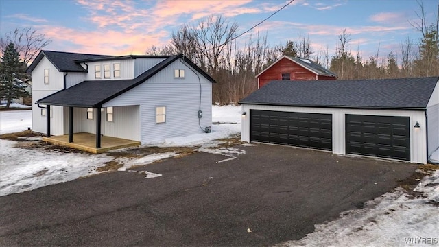 view of snow covered exterior featuring roof with shingles and a detached garage