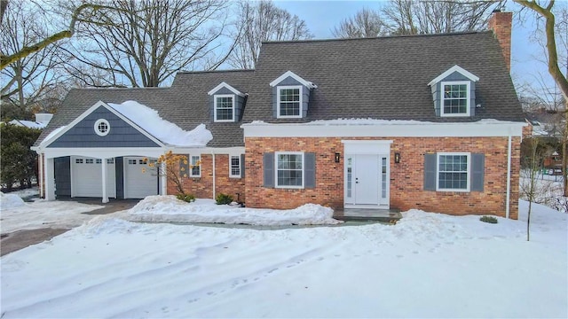 new england style home featuring driveway, a shingled roof, a chimney, an attached garage, and brick siding