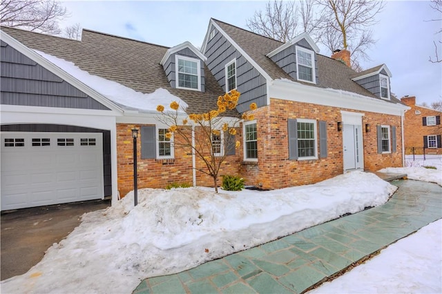 cape cod house featuring brick siding, roof with shingles, a chimney, a garage, and driveway