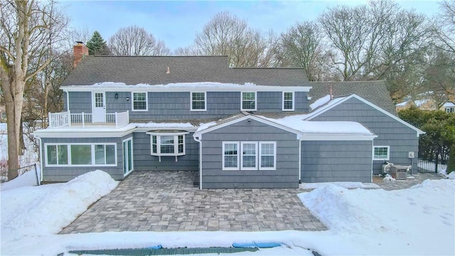 snow covered property with a chimney, cooling unit, and a balcony