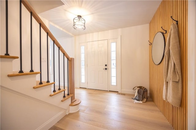 foyer with light wood finished floors, visible vents, stairs, and baseboards