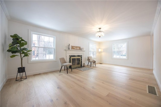 sitting room with visible vents, light wood-type flooring, a high end fireplace, and a healthy amount of sunlight