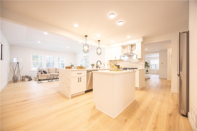 kitchen featuring pendant lighting, light countertops, appliances with stainless steel finishes, wall chimney range hood, and a peninsula