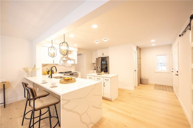 kitchen featuring light wood finished floors, white cabinets, a peninsula, pendant lighting, and a sink