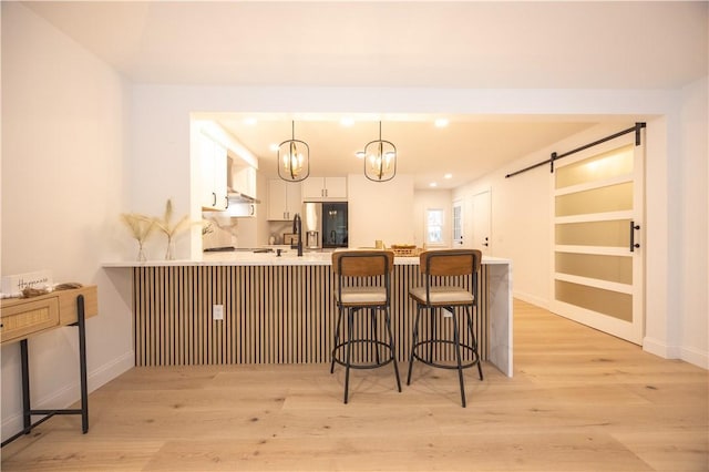 kitchen featuring a peninsula, a barn door, light countertops, and white cabinets