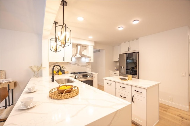 kitchen with white cabinets, wall chimney exhaust hood, appliances with stainless steel finishes, light stone counters, and a sink