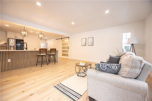 living area featuring light wood-type flooring, a barn door, baseboards, and recessed lighting