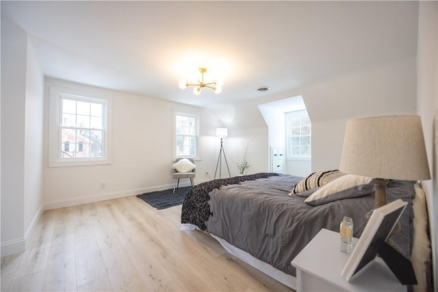 bedroom featuring baseboards, light wood finished floors, and an inviting chandelier