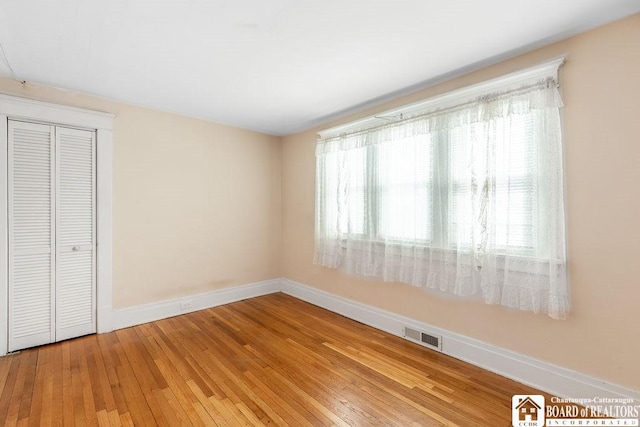 unfurnished bedroom featuring hardwood / wood-style flooring, visible vents, baseboards, and a closet