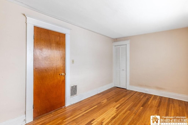 unfurnished room featuring hardwood / wood-style floors, visible vents, and baseboards