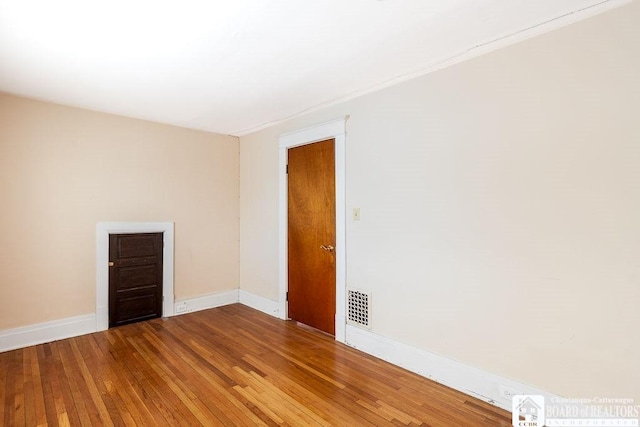 unfurnished room with wood-type flooring, visible vents, and baseboards