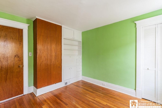 unfurnished bedroom with visible vents, a closet, hardwood / wood-style flooring, and baseboards