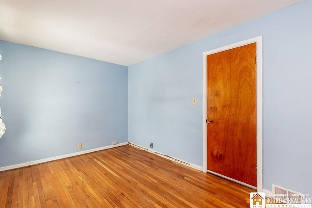 unfurnished room featuring wood-type flooring, visible vents, and baseboards