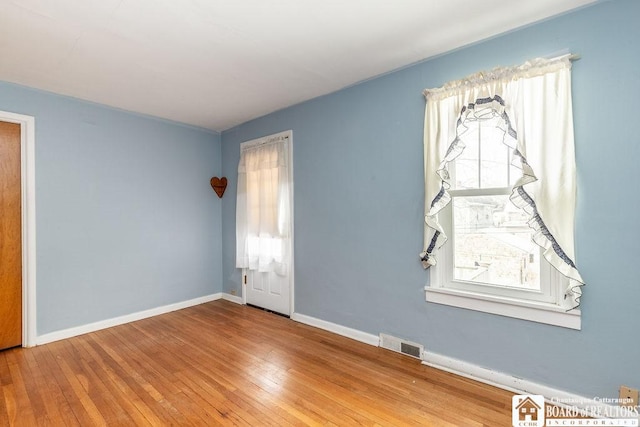 empty room with hardwood / wood-style flooring, visible vents, and baseboards