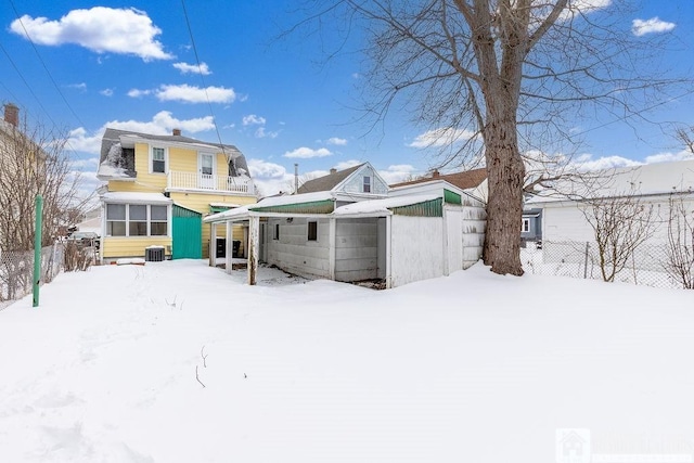 snow covered house with a balcony, a sunroom, fence, and central AC