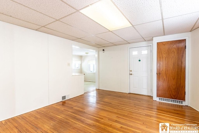 empty room with light wood-style floors, visible vents, and a drop ceiling