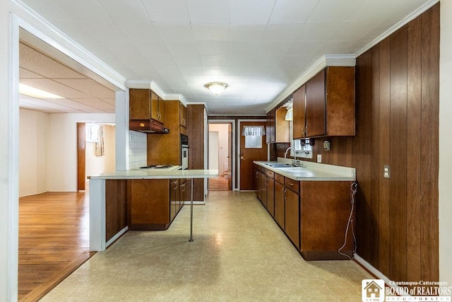 kitchen featuring white stovetop, wood walls, a sink, light countertops, and light floors