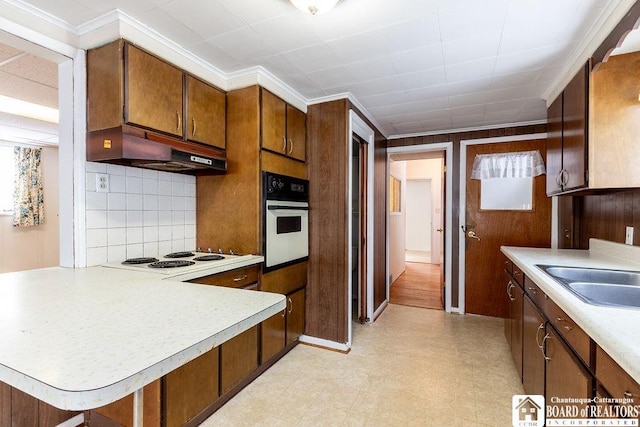 kitchen featuring light countertops, brown cabinetry, a sink, white appliances, and under cabinet range hood