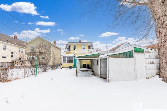 snow covered back of property featuring a garage and fence